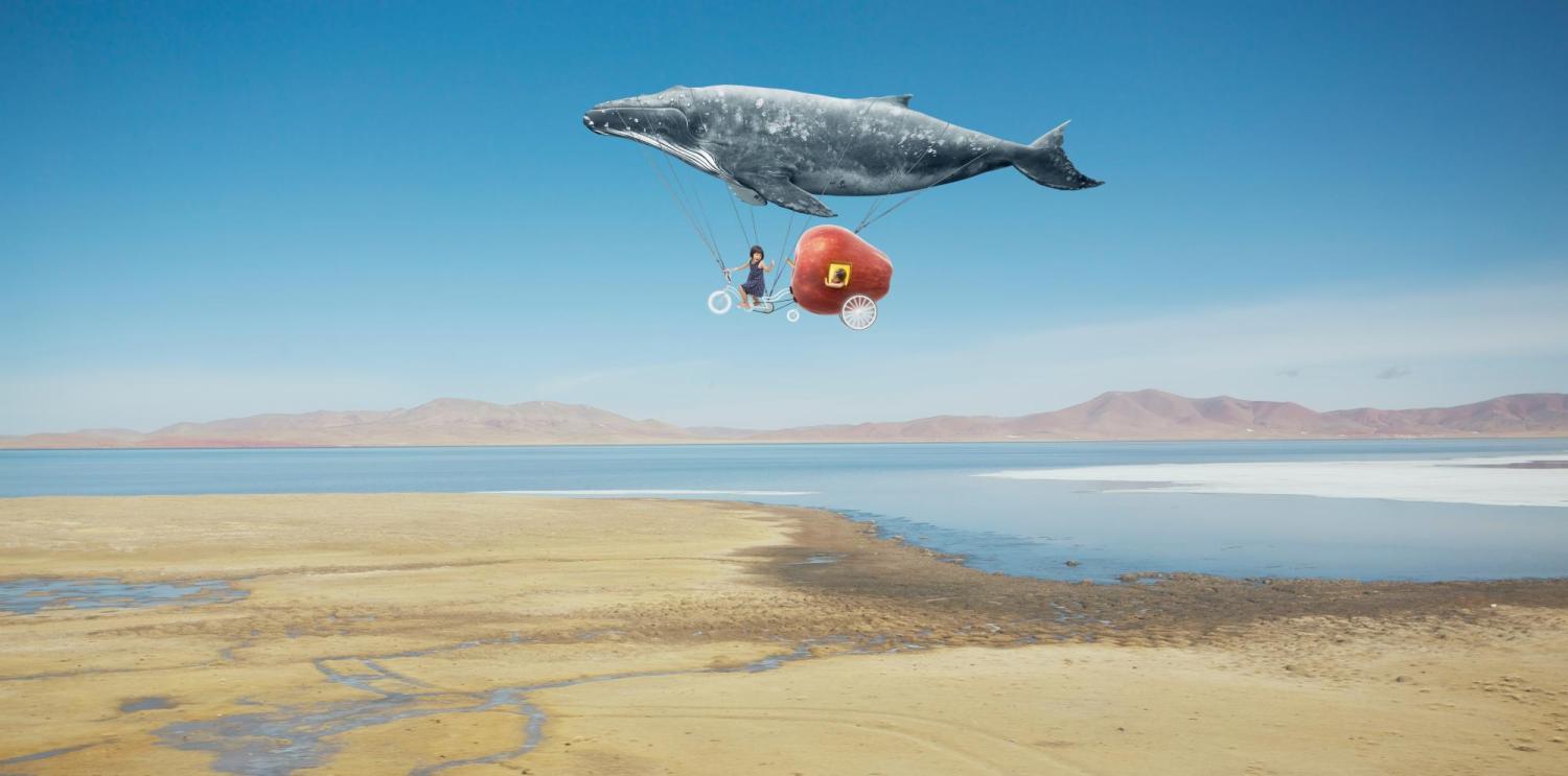 whale suspended by hot air balloon in blue sky over desert