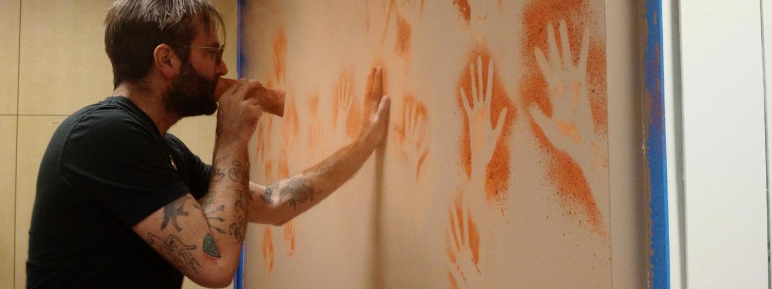 Man painting hand figures on a wall.