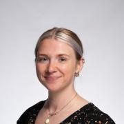 Nell Rosenthal headshot of blonde hair tucked back and wearing black top