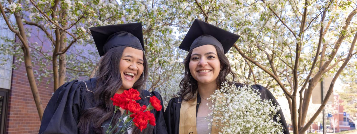 Two female graduates in their robes holding flowers.