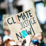 Photo of a hand holding a poster with the words climate justice now on it.