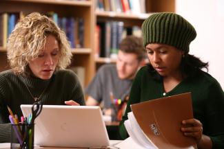 Two people looking at a laptop and papers