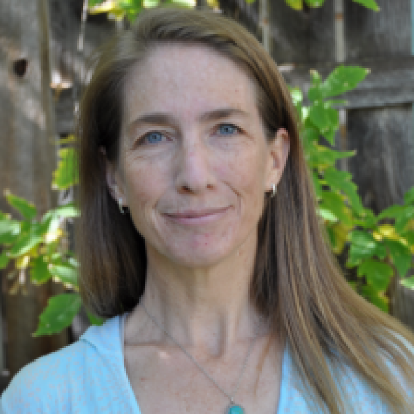 Woman with long light brown hair wearing blue t-shirt and blue necklace