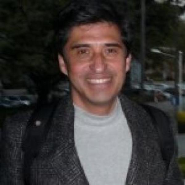 Man with short dark hair smiling wearing backpack and a grey blazer