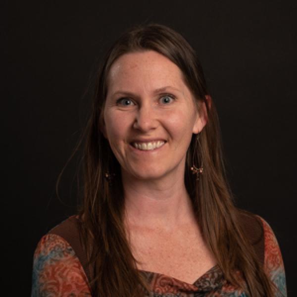 Headshot of woman with long brown hair wearing red and blue and brown printed shirt