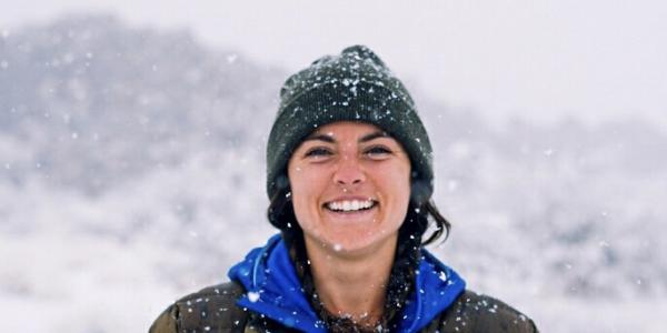 Young woman smiling with snowflakes falling around here in a green hat and a brown jacket