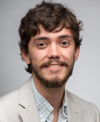 Headshot of man with brown hair and a bear and moustache smiling wearing a cream blazer against a white background