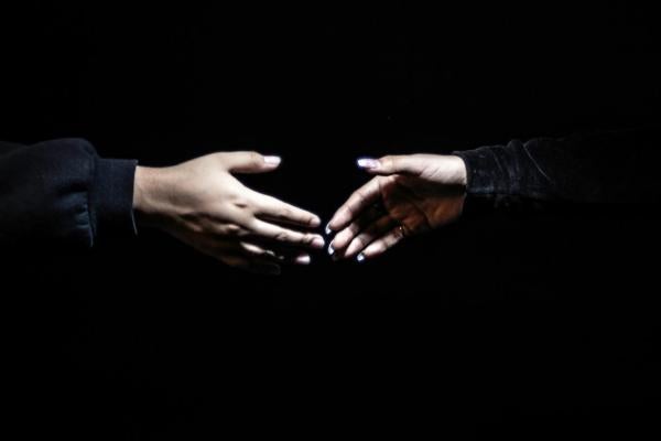 Two hands reaching towards each other in a dark setting, appearing to be on the verge of a handshake or connection.