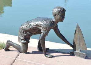 A statue of a child squatting near a toy sailboat