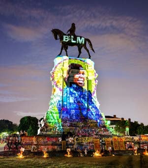 A large statue of a man on a horse is illuminated by a projection of the Black Lives Matter text.