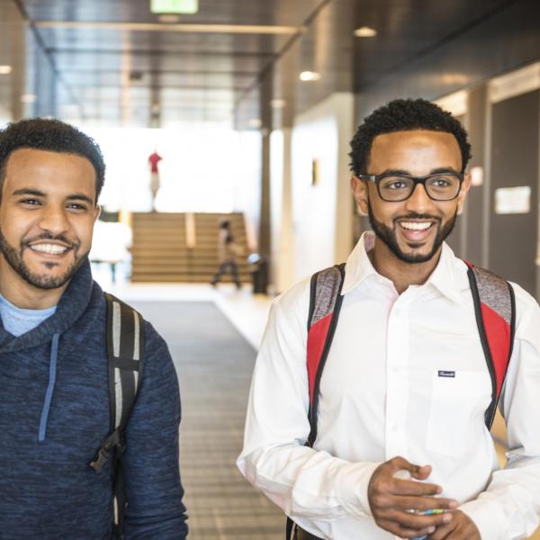 Two men smiling and walking through a campus building hallway