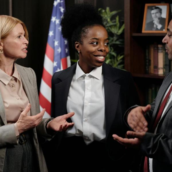 Group of professionals in formal attire having a discussion indoors with a U.S. flag in background