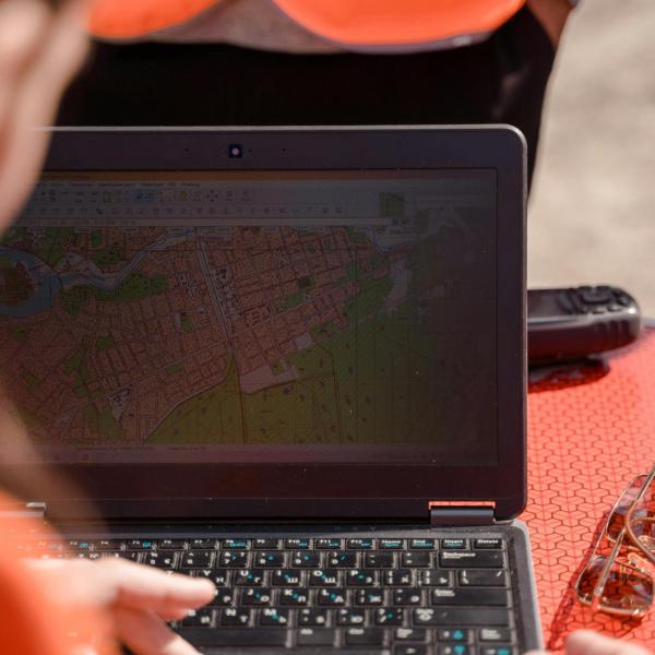 Person using a laptop displaying a detailed map, with others nearby wearing high-visibility vests.