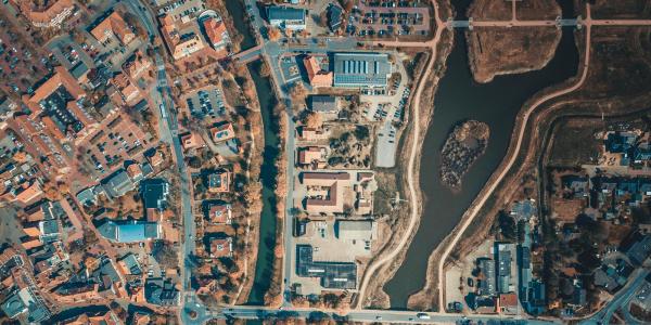 Aerial view of a small European city bisected by a winding river, showing dense residential neighborhoods, roads, bridges, and open green spaces in autumn.