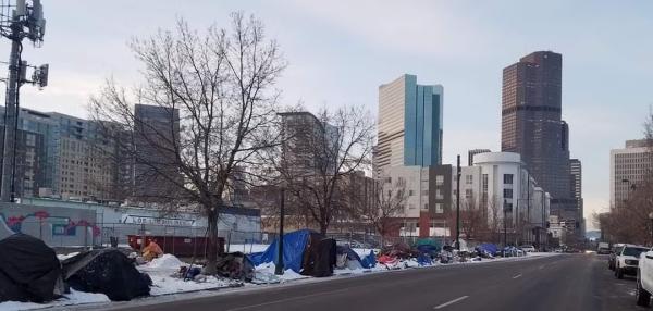 A homeless encampment in down town Denver. Tents and sleeping bags are lined up along the road. There is snow on the ground. 