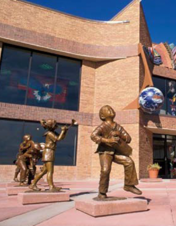 Statues of children playing instruments. One child is hitting a drum and another is blowing a horn.