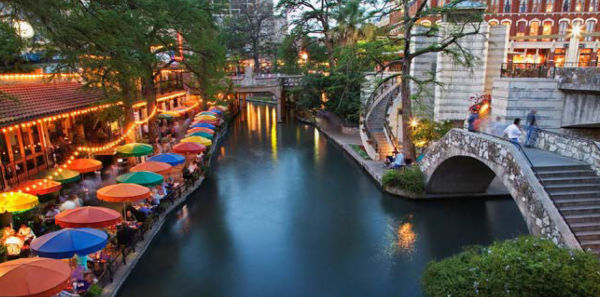 Scenic view of the San Antonio Riverwalk, featuring lush greenery, walkways, and vibrant shops along the river.