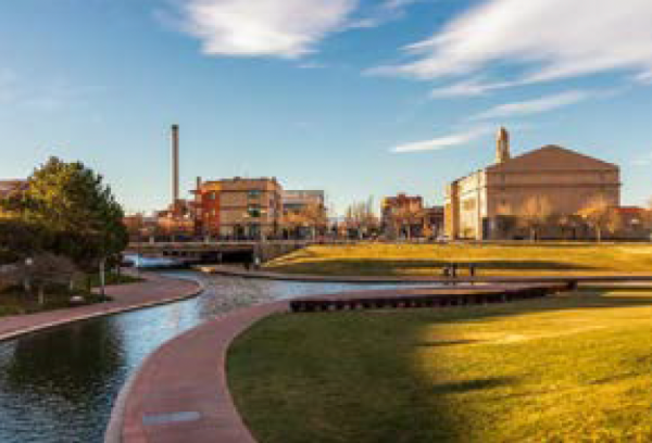 Pueblo's Riverwalk park canal surrounded by lush trees and modern buildings in the background.