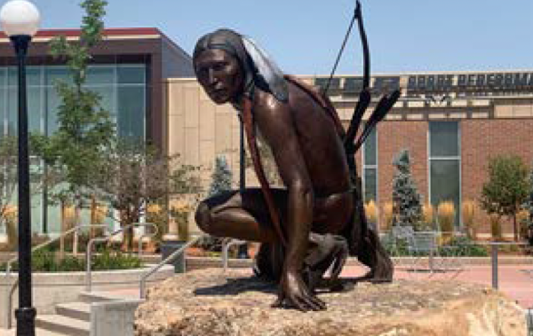 A Comanche man kneeling and holding a bow and arrows.