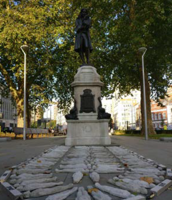 A statue of a woman, surrounded by stone figures lying on the ground in front of her.