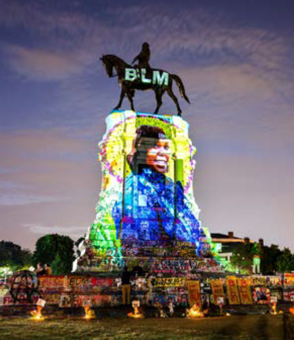 A large statue of a man on a horse is illuminated by a projection of the Black Lives Matter text.