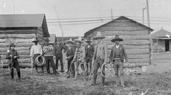 Black and white image from the Colorado History Museum depicting some of the first white settlers in the state standing among traditional log cabins.