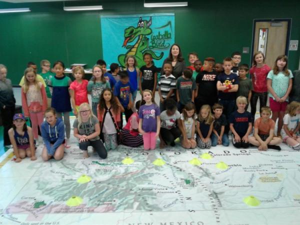 Young students posing for a photo on top of a giant map of Colorado