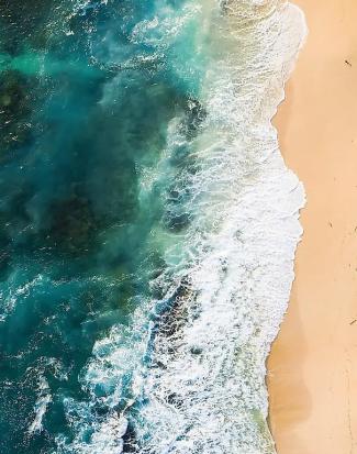 Aerial view of turquoise waves crashing on a sandy beach. The vibrant water contrasts with the soft, golden sand, evoking a sense of tranquility.