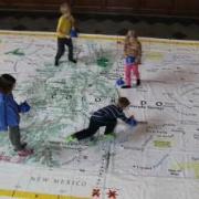 Four young children playing and exploring on a large floor map of Colorado and surrounding states.