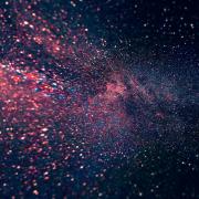 Colorful star field in deep space with pink, purple, and blue hues, creating a swirling galaxy effect against a dark background.