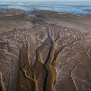Aerial view of river channels and tributaries branching through a dry, barren landscape, leading towards a distant body of water.
