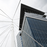 Low-angle view of two modern glass skyscrapers with a central white pole and cables forming a geometric pattern against a cloudy sky. Urban and architectural theme.