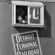 Black and white photo of a person looking out the window of a Detroit Terminal Railroad train car.