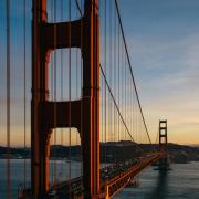 Golden Gate Bridge at sunset, with orange towers and suspension cables stretching over the water and light traffic crossing. Photo by Rockwell branding agency on Unsplash.