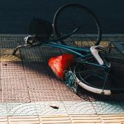 A teal bicycle lying on its side on a decorative tiled sidewalk, with a bright red plastic bag caught in the rear wheel. Obtained from Unsplash.