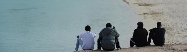 Photo of migrant men sitting on beach 