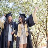 Stock photo of two women in graduation gowns celebrating