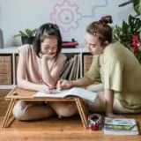 Two girls studying together while sitting on the floor looking at papers
