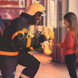 Fireman holding a teddy bear with a little girl standing in front of him
