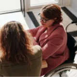 Two women working at a computer, one of whom is in a wheelchair