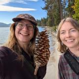 Abby and Dani are holding a very large pine cone on the shores of South Lake Tahoe