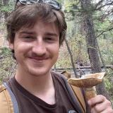 Will is holding a mushroom while standing outside in a forest
