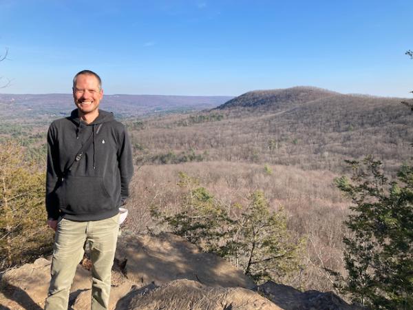 Nate wearing a fleece standing on a rock overlooking the mountains