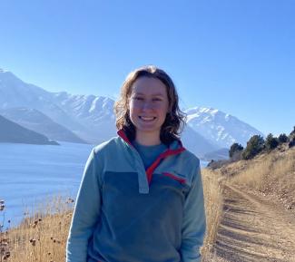 Anna standing on a trail near a lake in front of a snow capped mountain