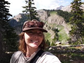 Self picture of Abby wearing a hat and sunglasses standing in the forrest