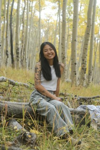 Kailtin sitting on a log in a yellow colored forest 