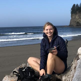 Abbigail sitting on a beach wearing a dark hoody