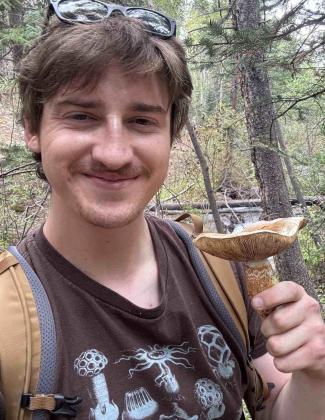 Will is standing in the forest holding a mushroom