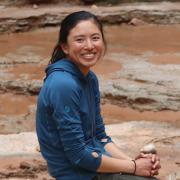 Lilly has dark hair wearing a blue hoodie sitting on rocks