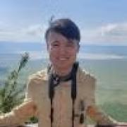 Paul with a camera around his neck standing on a mountain overlooking the ocean